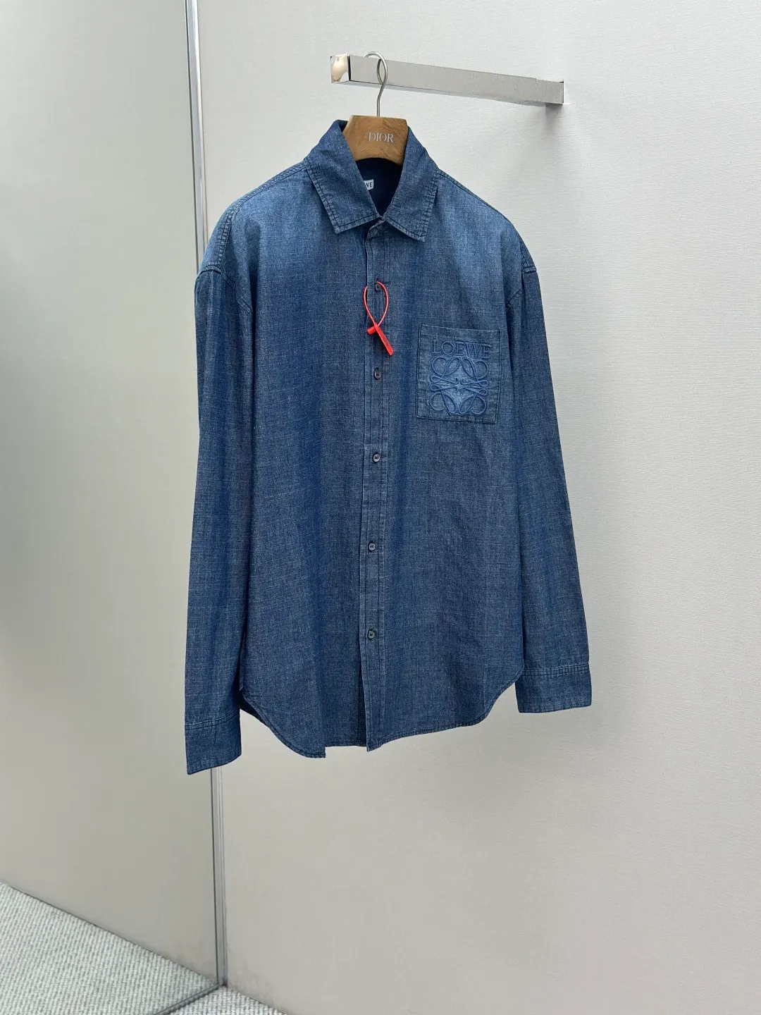 P430 Loewe Anagram Gradient Embroidered Pocket Shirt Made of custom-made high-quality cotton chambray fabric, with a unique washed gradient blue as the main tone, from dark to light and from thick to light. The chest patch pocket is decorated with Loewe Anagram embroidery as its soul, engraved with LOEWE-style casual elegance, and the natural and smooth lines show the casualness.  Imported embroidery machines are used, and advanced computer control systems and precision mechanical components are used to realize Loewe embroidery operations.  The gradient dynamic spray dyeing process uses specialized spray dyeing equipment to accurately spray dye onto the surface of the fabric in the form of mist (by accurately controlling the different dimensions of the spray of the spray dyeing equipment, combined with the movement speed and direction during the dyeing process) to present a smooth and natural transition effect of color. The butterfly rhyme pinch pleating body dart technology is inspired by the beautiful shape of butterflies, and uses precise pinch pleating techniques to create a flexible pleat effect like butterfly wings on the garment, making the garment fit more closely to the body.  size:44.46.48.50
